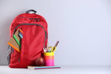 Işık duvarının yanındaki masada farklı kırtasiye malzemelerinin olduğu kırmızı sırt çantası. Metin için boşluk