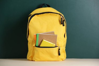 Tahtanın yanındaki masada defterleri olan sarı sırt çantası.