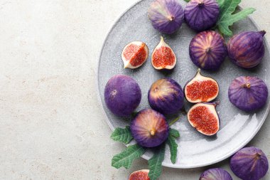 Taze incir ve yeşil yapraklar gri desenli masada, düz yerde. Metin için boşluk