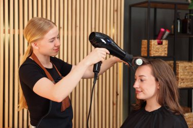 Kuaför kuaförde müşterinin saçını kurutuyor.