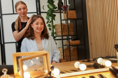 Kuaför, kuaför salonundaki aynanın yanında müşteriyle çalışıyor.