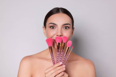 Açık gri arka planda makyaj fırçası olan güzel bir kadın.