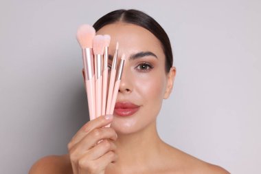 Açık gri arka planda makyaj fırçası olan güzel bir kadın.