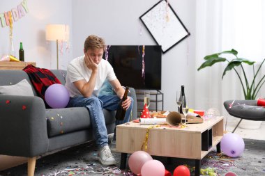 İçki şişesi olan bir adam partiden sonra dağınık bir odada kanepede akşamdan kalma.