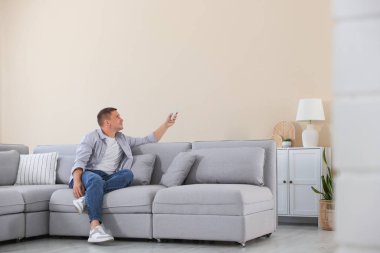Evdeki kanepede uzaktan kumandayla klima kullanan bir adam.