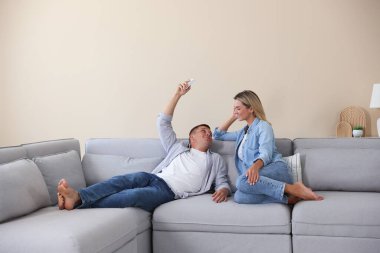 Kadın ve erkek evdeki kanepede klimayı kontrol etmek için uzaktan kumanda kullanıyorlar.