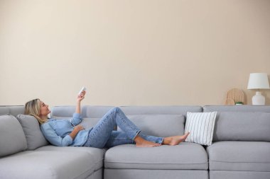 Evdeki koltukta uzaktan kumandayla klima kullanan bir kadın.