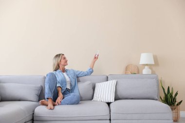 Evdeki koltukta uzaktan kumandayla klima kullanan bir kadın.