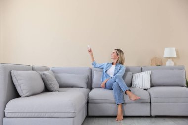 Evdeki koltukta uzaktan kumandayla klima kullanan bir kadın.