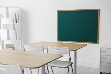 Boş yeşil karatahta, masalar, sandalyeler ve raf ünitesi sınıfta.