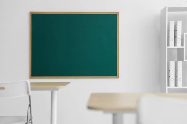 Boş yeşil karatahta, masalar, sandalyeler ve raf ünitesi sınıfta.