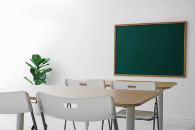 Boş yeşil karatahta, masalar, sandalyeler ve bitkiler sınıfta