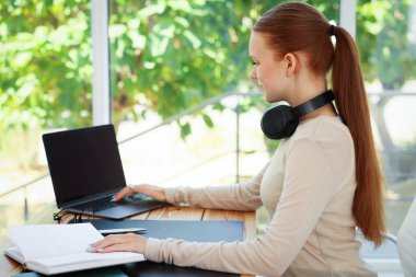 Kitapları olan genç bir kız, bilgisayarını içeride, ahşap masada kullanıyor. Ev işyeri