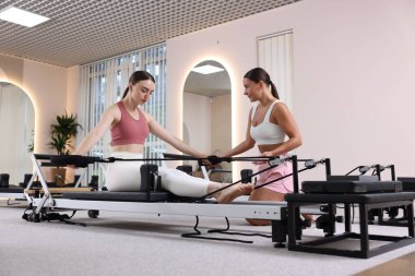 Stüdyoda pilates eğitmeni tarafından yönetilen reformcu kadın üzerinde egzersiz yapıyor.