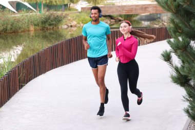 Nehir kenarında koşan kulaklıklı, gülümseyen bir çift.