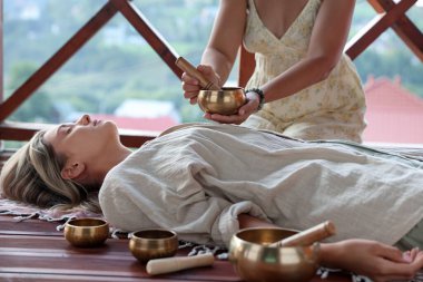 Şarkı söyleyen kadın kase terapisi görüyor. Kapalı yerde yatıyor.