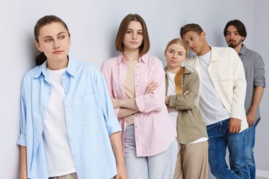 Açık gri duvarın yanında bir grup insan bekliyor.