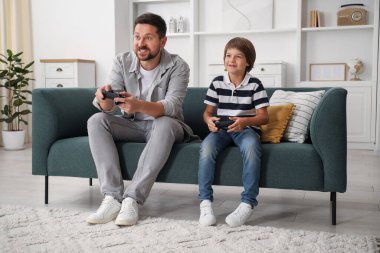 Evde kanepede video oyunu oynayan kontrolörlü baba ve oğul.
