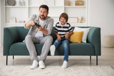 Evde kanepede video oyunu oynayan kontrolörlü baba ve oğul.