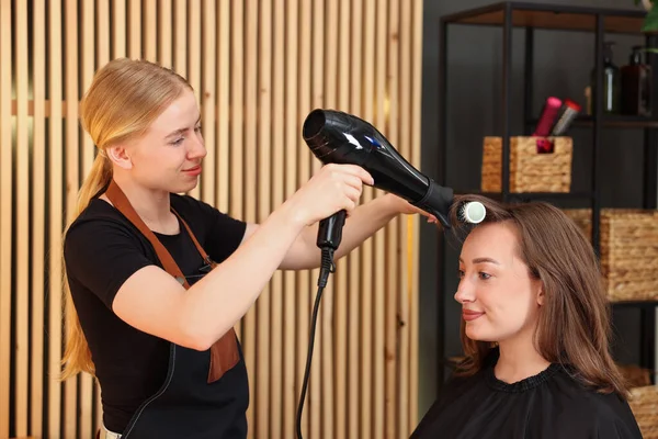 Kuaför kuaförde müşterinin saçını kurutuyor.