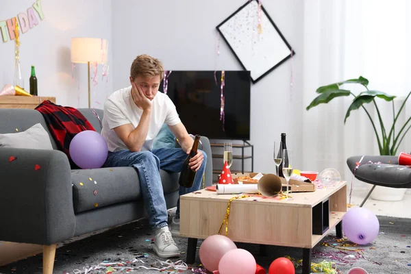 İçki şişesi olan bir adam partiden sonra dağınık bir odada kanepede akşamdan kalma.