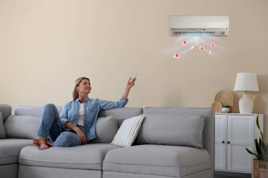 Evdeki koltukta uzaktan kumandayla klima kullanan bir kadın.