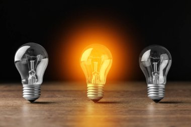 Fikir kavramı. Diğerlerinin arasında parlayan bir ampul, siyah arka plana karşı ahşap masada.