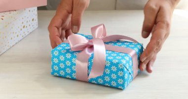 Beyaz ahşap masada güzel fiyonklu hediye kutusunu açan kadın, yakın plan.