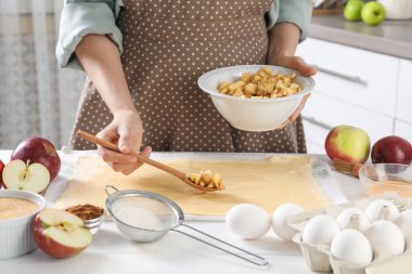 Elmalı turta yapıyorum. Mutfaktaki masada meyveleri hamura koyan kadın, yakın plan.