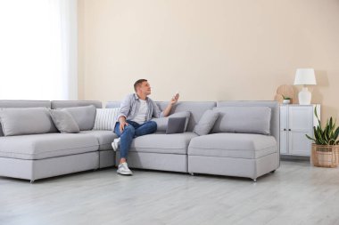 Evdeki kanepede uzaktan kumandayla klima kullanan bir adam.