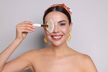 Açık gri arkaplanda makyaj fırçası olan güzel bir kadın.