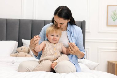 Mother kissing her cute baby on bed at home