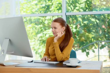 İçerideki ahşap masada bilgisayar kullanan genç bir kız. Ev işyeri