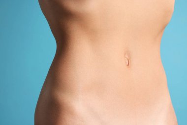 Açık mavi arka planda düz göbekli kadın, yakın plan.