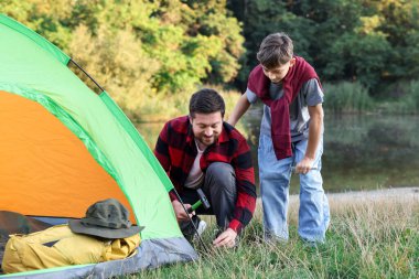 Baba ve oğul nehir kenarında kamp çadırı kuruyorlar.