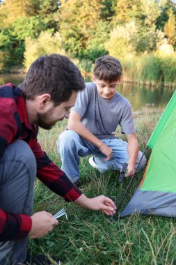 Baba ve oğul dışarıda kamp çadırı kuruyorlar.
