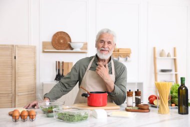 Mutfaktaki beyaz mermer masada yaşlı bir adam yemek pişiriyor.