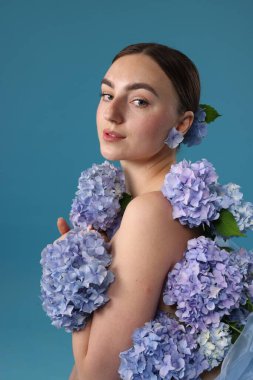 Mavi arka planda hortensiya çiçekleri olan güzel genç bir kadın.