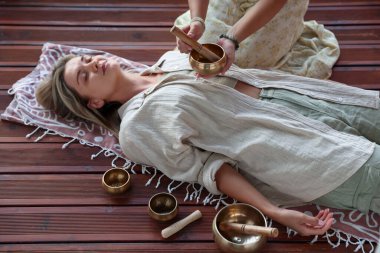 Şarkı söyleyen kadın kase terapisi görüyor. Kapalı yerde yatıyor.