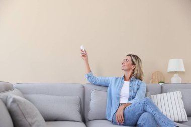 Evdeki koltukta uzaktan kumandayla klima kullanan bir kadın.