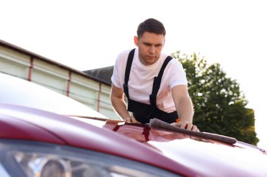 Adam arabanın kaputunu gri mikrofiber bezle siliyor.