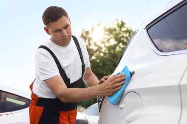 Dışarıdaki mavi mikrofiber bez parçasıyla araba silen adam.