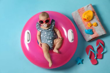 Güneş gözlüklü şirin bir bebek. Şişirilebilir yüzüğü ve açık mavi arka planda plaj aksesuarları var.