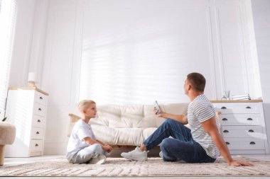 Evdeki klimayı kontrol etmek için uzaktan kumanda kullanan sevimli bir çocuk ve babası var.