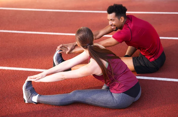 Stadyumda koşmadan önce spor giyimli çift esneme hareketleri yapıyor.