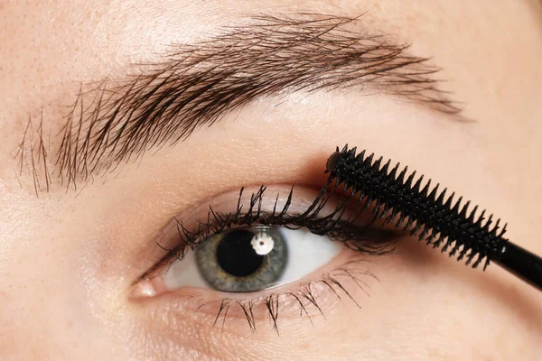 Bir kadın kirpiklerine rimel sürüyor, yakın plan.