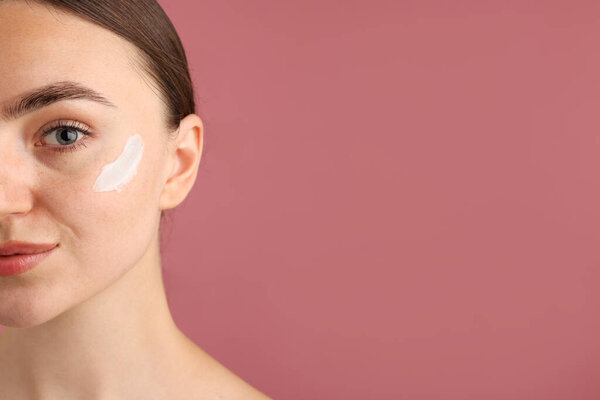 Beautiful woman with cream on her face against pink background, closeup. Space for text