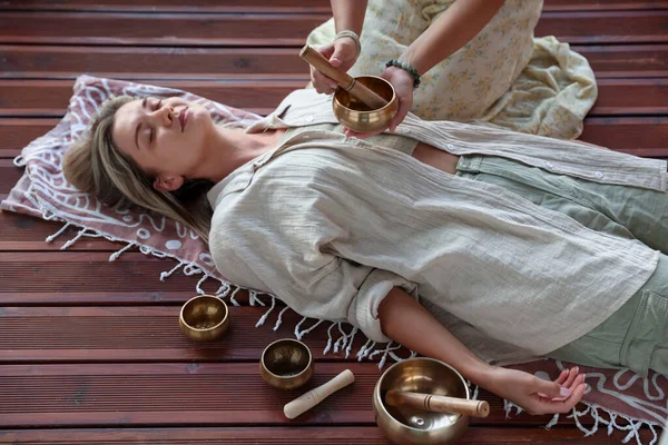 Şarkı söyleyen kadın kase terapisi görüyor. Kapalı yerde yatıyor.