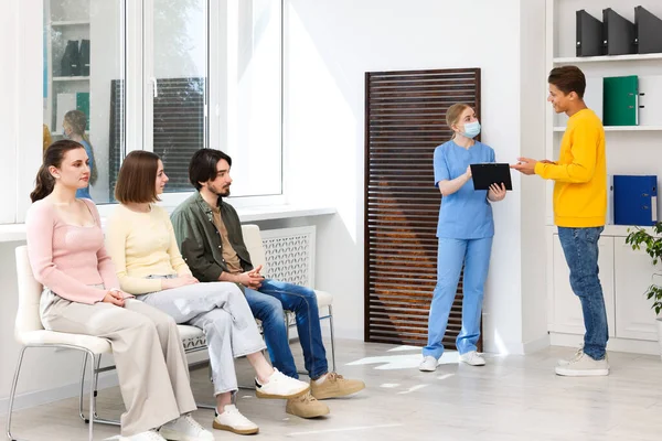 İnsanlar hastanede sandalyelerde kuyrukta bekliyorlar.