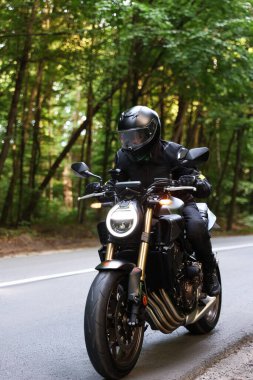 Kasklı genç adam modern motosikleti açık havada kullanıyor.